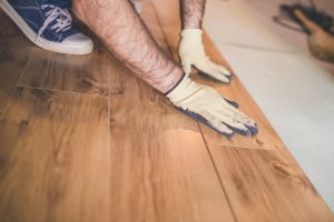 Close-up of a person installing hybrid flooring, showing hands in protective gloves fitting wood-look planks together, emphasizing the types of hybrid flooring available for home improvement.