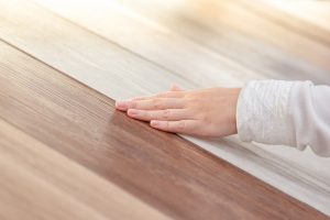 Close-up of a hand touching different types of hybrid flooring, showcasing various wood-look finishes, emphasizing the texture and variety available in hybrid flooring options.