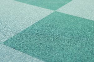 Close-up of green carpet tiles in need of regular vacuuming to keep them clean and prolong their lifespan.